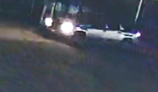 Dark camera footage photo of suspect's vehicle with headlights turned on. 